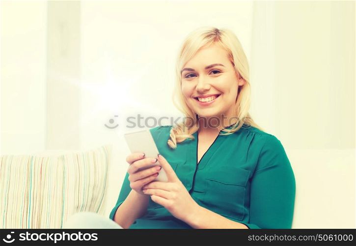 people, technology, communication and leisure concept - happy young woman sitting on sofa with smartphone at home. happy woman with smartphone at home