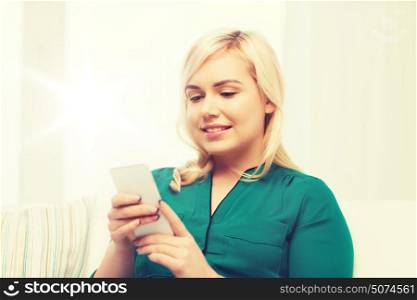 people, technology, communication and leisure concept - happy young woman sitting on sofa with smartphone at home. happy woman with smartphone at home