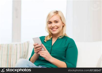 people, technology, communication and leisure concept - happy young woman sitting on sofa with smartphone at home