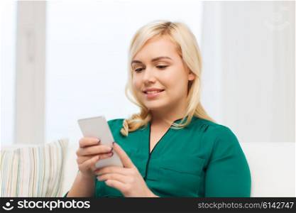 people, technology, communication and leisure concept - happy young woman sitting on sofa with smartphone at home