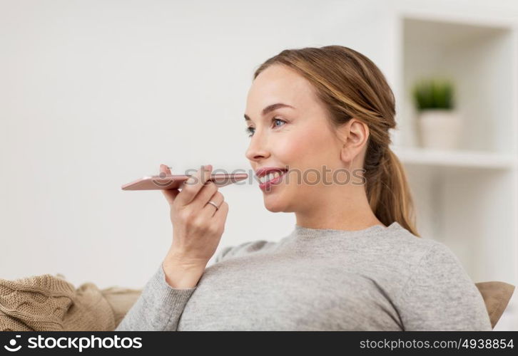 people, technology, communication and leisure concept - happy young woman using voice command recorder or calling on smartphone at home. woman using smartphone voice command recorder