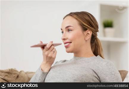 people, technology, communication and leisure concept - happy young woman using voice command recorder or calling on smartphone at home. woman using smartphone voice command recorder