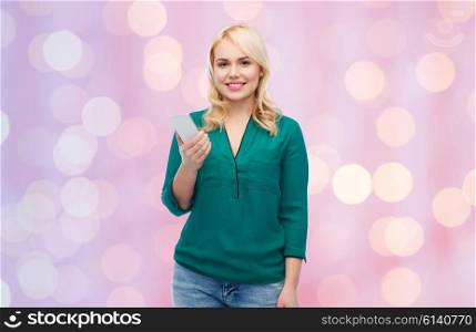people, technology, communication and leisure concept - happy young woman with smartphone over pink holidays lights background