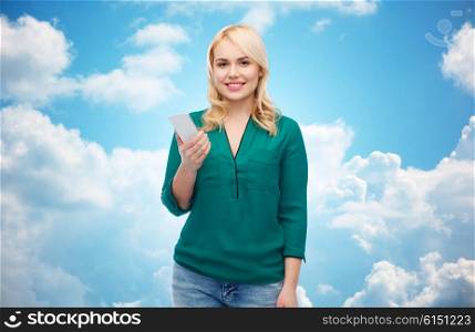 people, technology, communication and leisure concept - happy young woman with smartphone over blue sky and clouds background