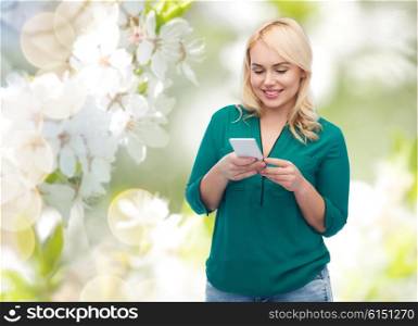 people, technology, communication and leisure concept - happy young woman with smartphone texting message over natural cherry blossom background