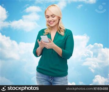 people, technology, communication and leisure concept - happy young woman with smartphone texting message over blue sky and clouds background