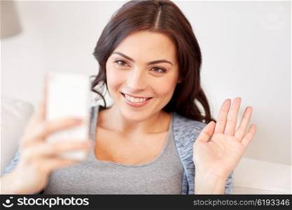 people, technology, communication and leisure concept - happy young woman with smartphone having video call and waving hand at home