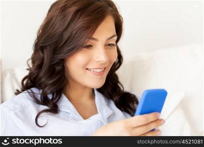 people, technology, communication and leisure concept - happy young woman with smartphone at home
