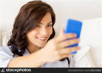 people, technology, communication and leisure concept - happy young woman with smartphone taking selfie at home