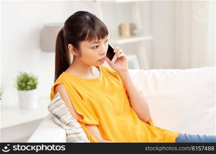 people, technology, communication and problem concept - young asian woman calling on smartphone at home