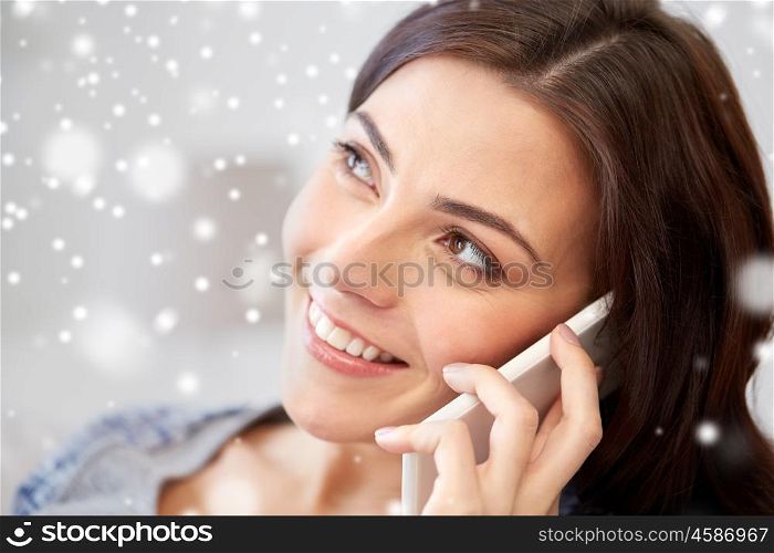 people, technology, communication and winter concept - happy young woman calling on smartphone at home over snow