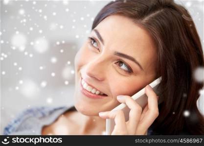 people, technology, communication and winter concept - happy young woman calling on smartphone at home over snow