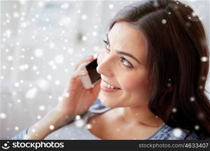 people, technology, communication, christmas and winter concept - close up of happy young woman calling on smartphone at home over snow