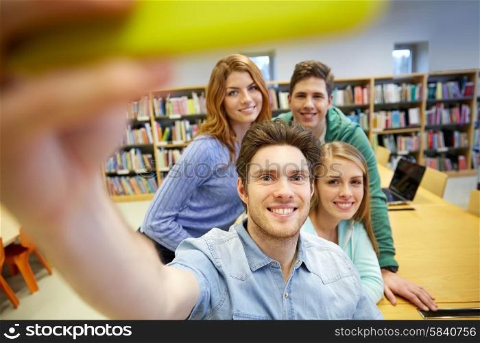 people, technology, education and school concept - happy students or friends with smartphone taking selfie in library