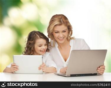 people, technology, family and parenthood concept - happy mother and daughter with laptop and tablet pc computers sitting at table over green background