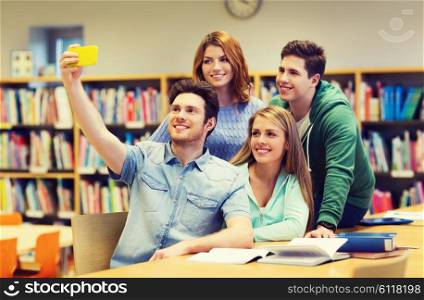 people, technology, friendship, education and school concept - group of happy students with smartphone taking selfie at library