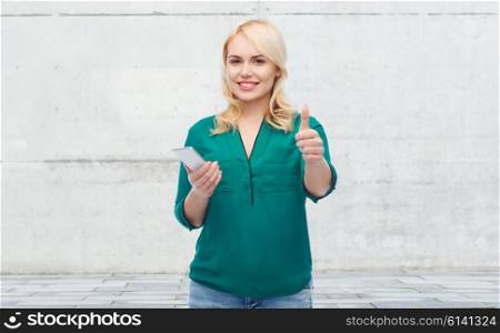 people, technology, gesture, communication and leisure concept - happy young woman with smartphone texting message over gray concrete wall background
