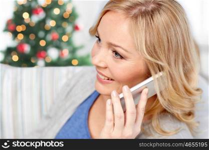 people, technology, holidays and communication concept - smiling woman calling on smartphone at home over christmas tree lights background