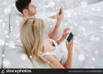 people, technology, internet addiction and communication concept - couple with smartphones texting in bed over snow