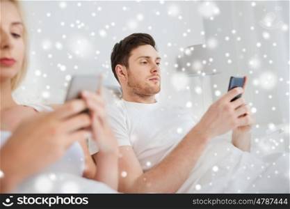 people, technology, internet addiction and communication concept - couple with smartphones texting in bed over snow