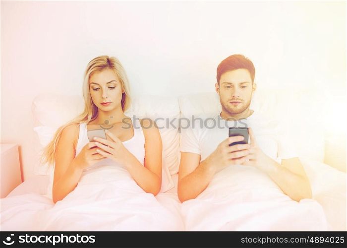 people, technology, internet and communication concept - couple with smartphones in bed