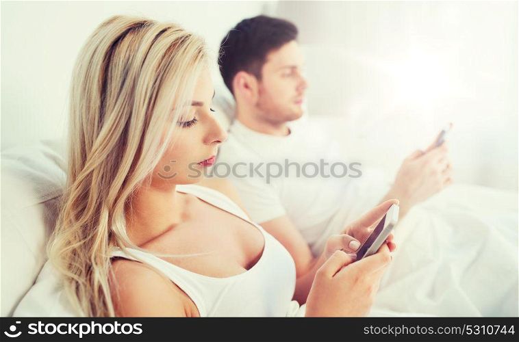 people, technology, internet and communication concept - couple with smartphones in bed. couple with smartphones in bed