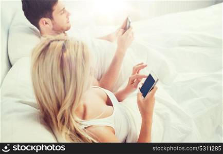 people, technology, internet and communication concept - couple with smartphones in bed. couple with smartphones in bed