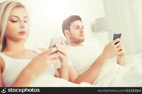 people, technology, internet and communication concept - couple with smartphones in bed. couple with smartphones in bed