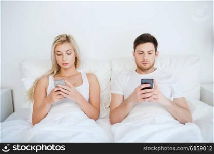 people, technology, internet and communication concept - couple with smartphones in bed