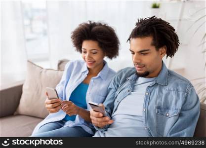 people, technology, internet and communication concept - happy couple with smartphones at home. happy couple with smartphones at home