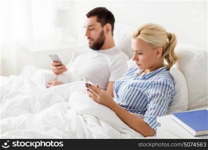 people, technology, internet, relations and communication concept - couple with smartphones in bed at home. couple with smartphones in bed at home