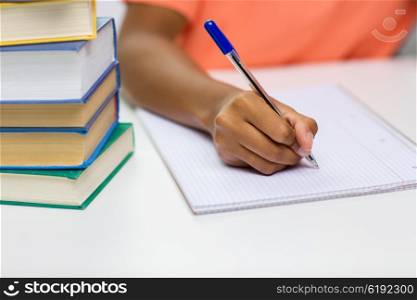 people, technology, learning and education concept - close up of african american young woman hand writing to notebook with books at home