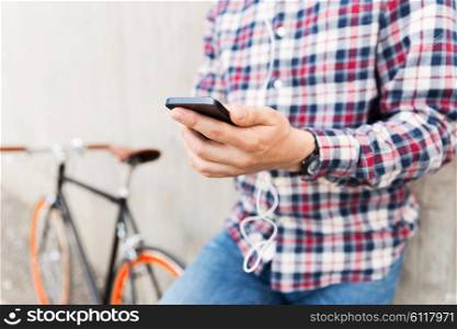 people, technology, leisure and lifestyle - close up of young hipster man in earphones with fixed gear bike listening to music on city street