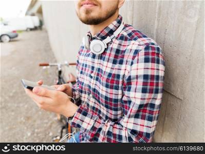 people, technology, leisure and lifestyle - close up of young hipster man with earphones, smartphone and fixed gear bike on city street