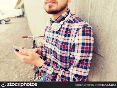 people, technology, leisure and lifestyle - close up of young hipster man with earphones, smartphone and fixed gear bike on city street