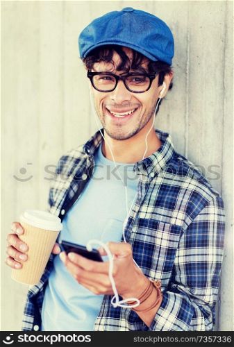 people, technology, leisure and lifestyle - man with earphones and smartphone drinking coffee and listening to music on city street. man with earphones and smartphone drinking coffee
