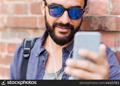 people, technology, leisure and lifestyle - man with earphones, smartphone and bag on city street and listening to music