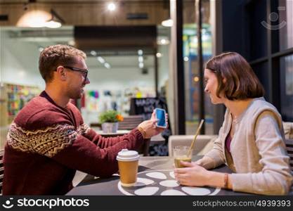 people, technology, lifestyle and dating concept - happy couple with smartphone drinking coffee and smoothie at cafe. happy couple with smartphone and drinks at cafe