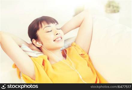 people, technology, relax and leisure concept - happy asian young woman lying on sofa with earphones listening to music at home. happy asian woman with earphones listening music. happy asian woman with earphones listening music