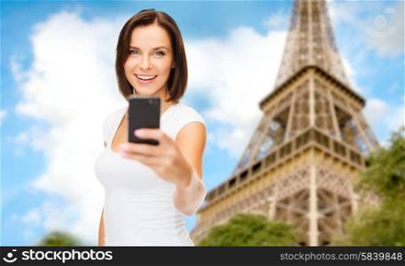 people, technology, tourism and travel concept - young woman taking selfie with smartphone over paris eiffel tower background