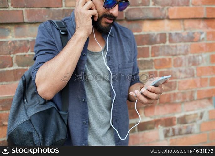 people, technology, travel and tourism concept - close up of man with earphones, smartphone and bag listening to music on street