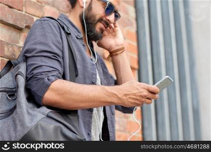 people, technology, travel and tourism concept - close up of man with earphones, smartphone and bag listening to music on street