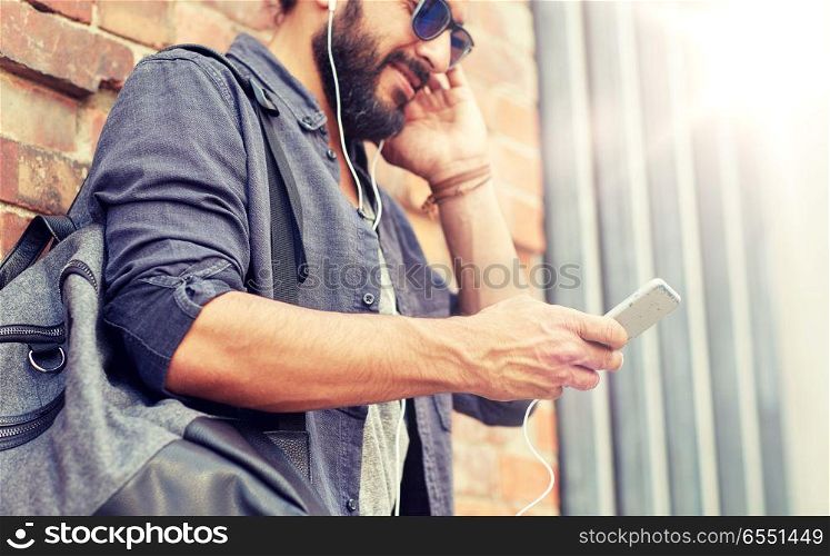 people, technology, travel and tourism concept - close up of man with earphones, smartphone and bag listening to music on street. man with earphones, smartphone and bag on street. man with earphones, smartphone and bag on street