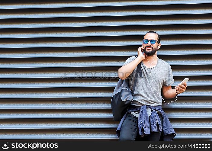 people, technology, travel and tourism - man with earphones, smartphone and bag on city street and listening to music