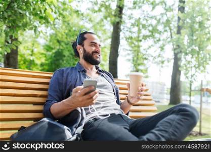 people, technology, travel and tourism - man with earphones, smartphone and bag sitting on city street bench and listening to music