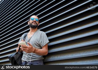 people, technology, travel and tourism - man with earphones, smartphone and bag listening to music on city street