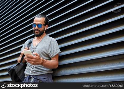 people, technology, travel and tourism - man with earphones, smartphone and bag listening to music on city street