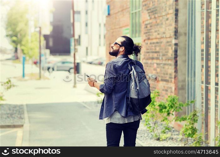 people, technology, travel and tourism - man with earphones, smartphone and bag walking along city street and listening to music . man with earphones and smartphone walking in city. man with earphones and smartphone walking in city