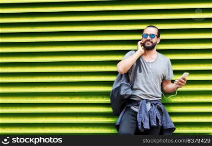 people, technology, travel and tourism - man with earphones, smartphone and bag on city street and listening to music over ribbed green wall background. man with earphones and smartphone over wall