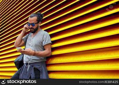 people, technology, travel and tourism - man with earphones, smartphone and bag on city street and listening to music over ribbed yellow wall background. man with earphones and smartphone over wall